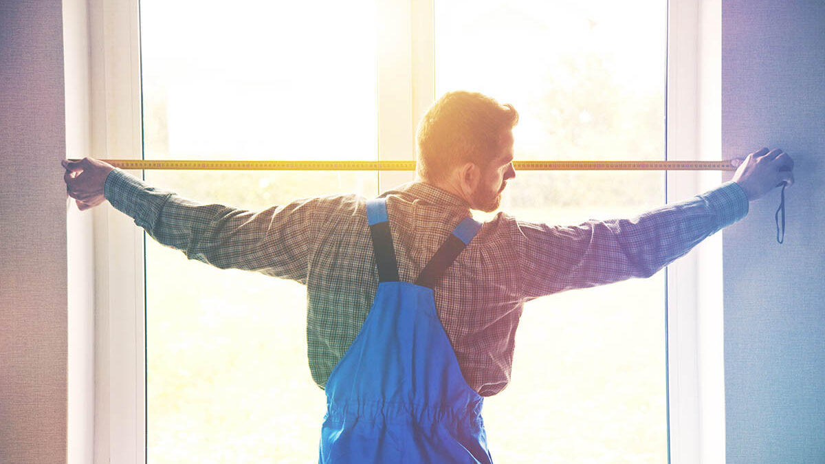 a person holds a tape measure next to a window after learning measuring for window replacement