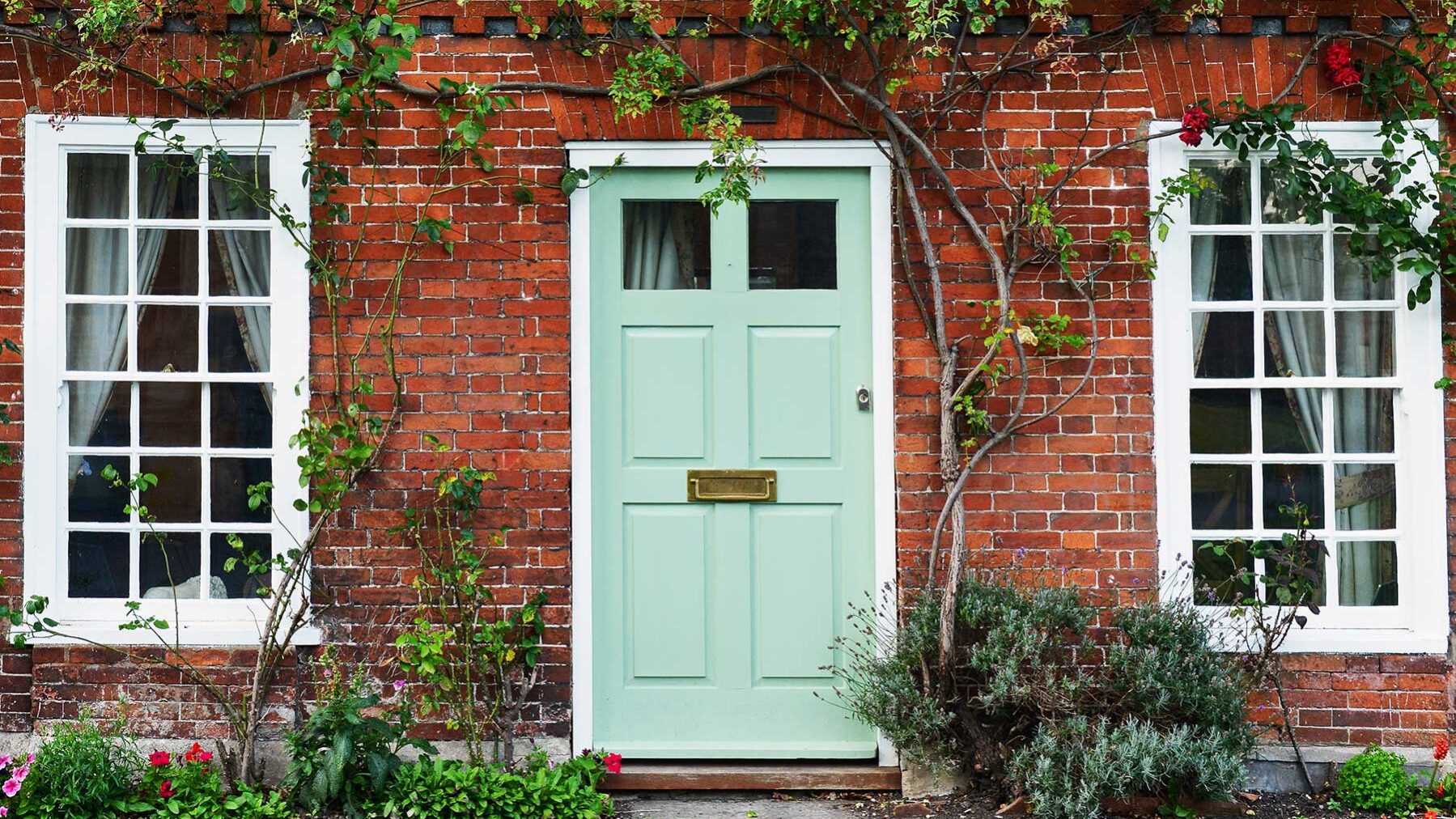 the lovely pastel green front door of a brick house with big windows and crawling ivy