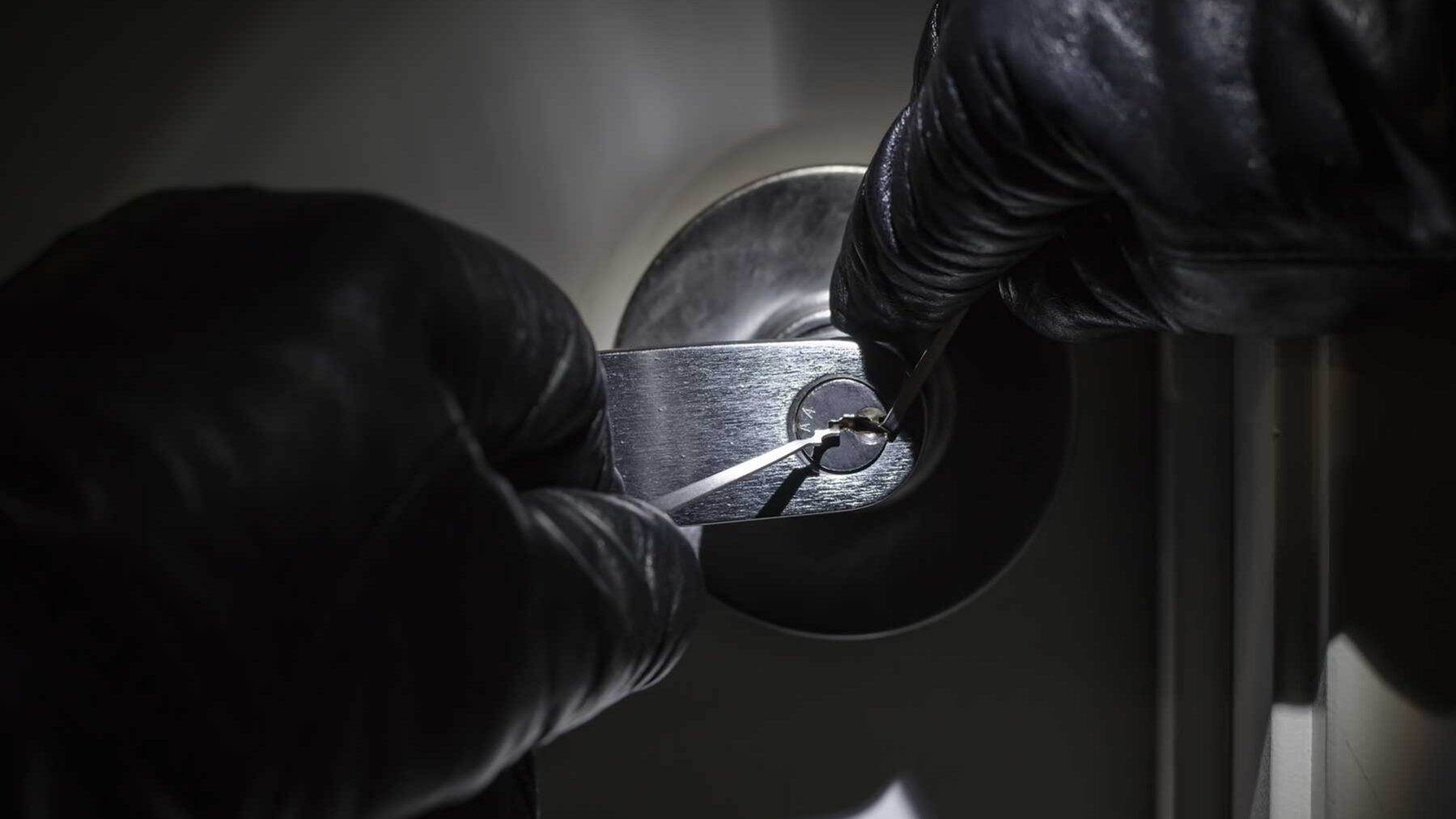a burglar uses a lock pick to break into the front door of a home