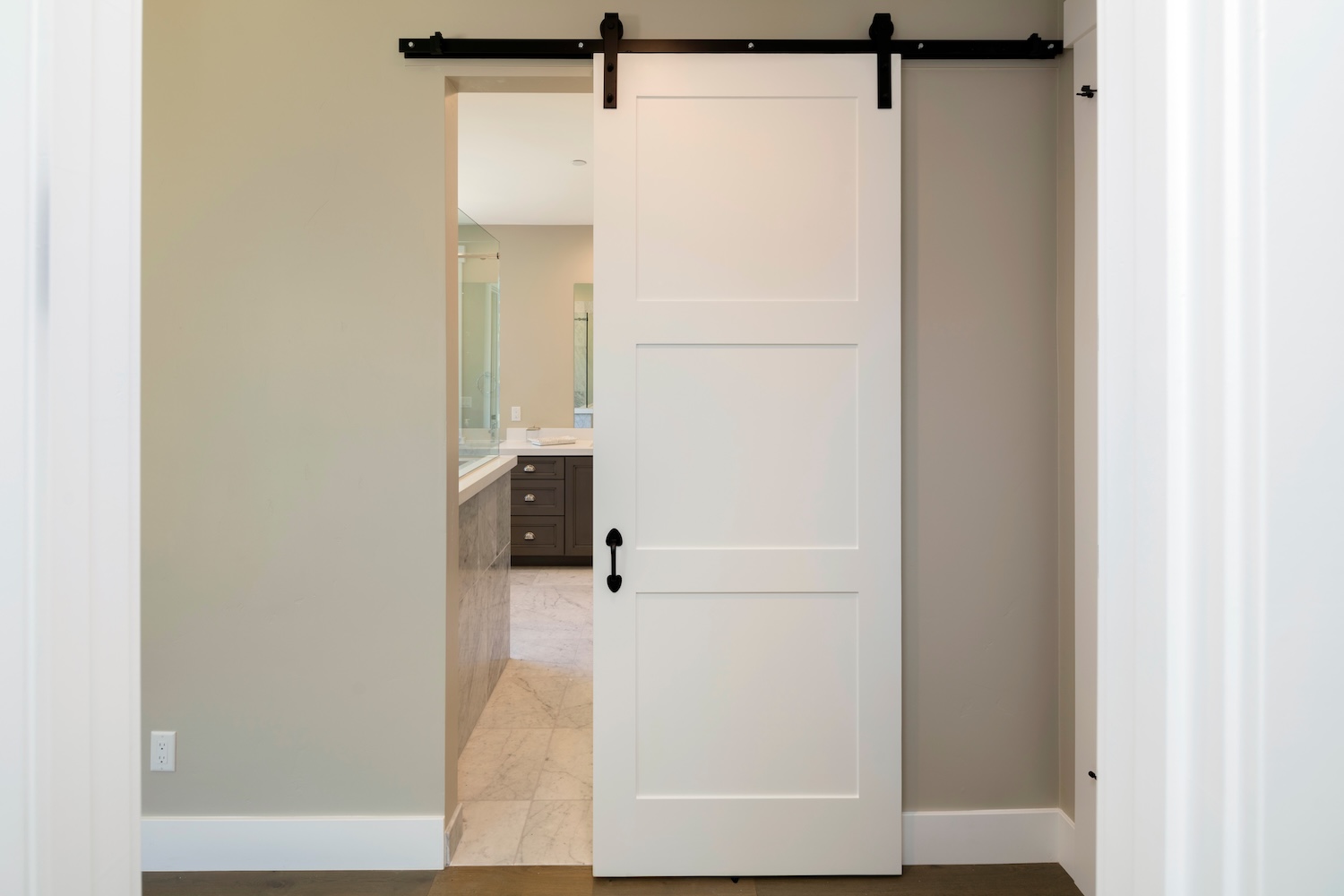 White sliding barn door partially open to reveal a modern bathroom with marble flooring and dark vanity