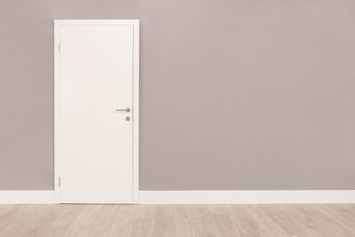 White modern flush door with a metal handle in a neutral beige room with light wood flooring