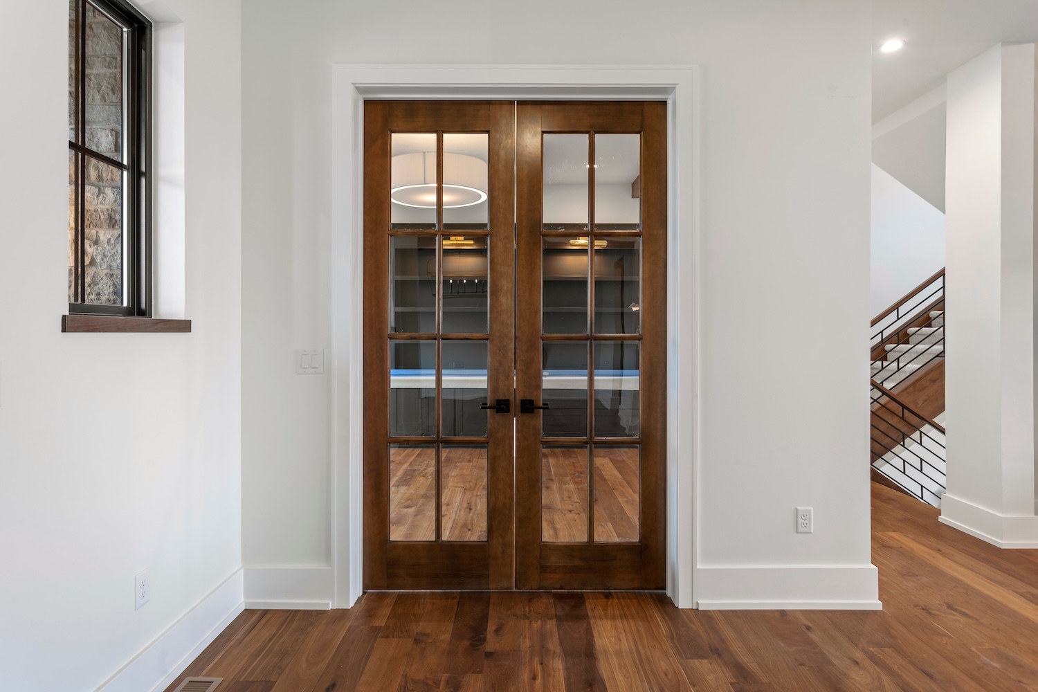 Double wooden French doors with glass panels opening to a room with hardwood floors and white walls.