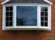 Exterior view of a brick home featuring a large white bay window with shingled roof.