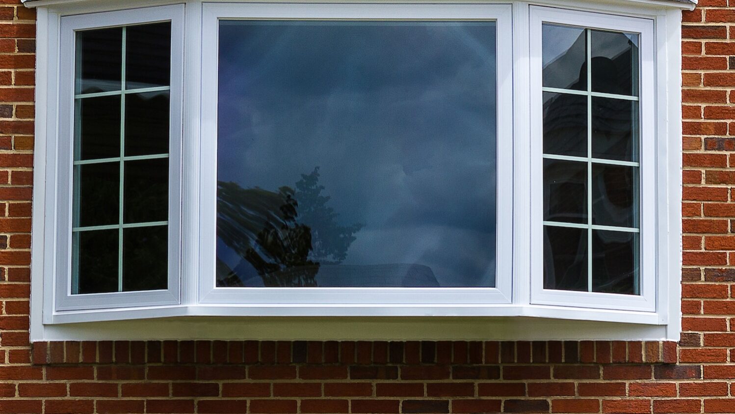 Exterior view of a brick home featuring a large white bay window with shingled roof.
