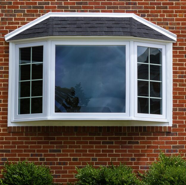 Exterior view of a brick home featuring a large white bay window with shingled roof.
