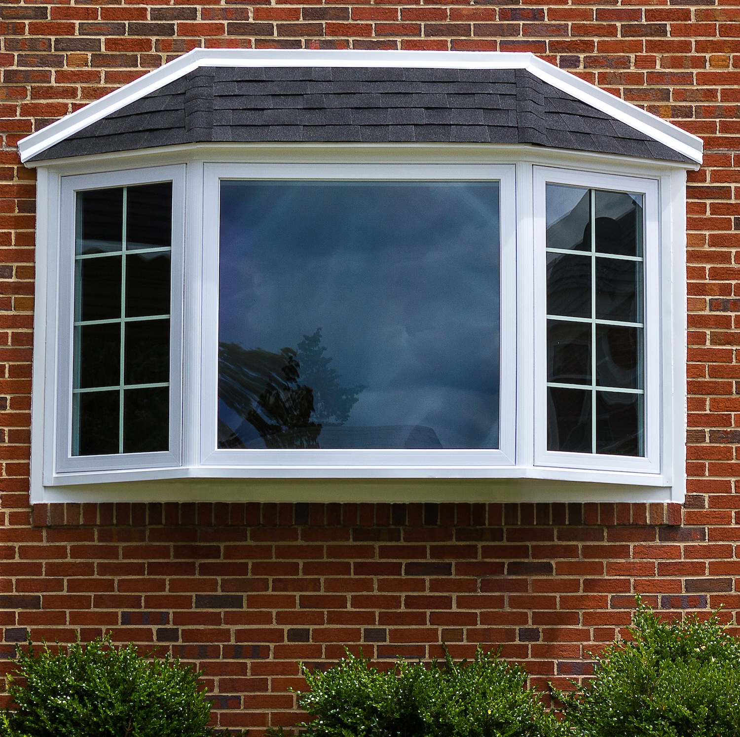 Exterior view of a brick home featuring a large white bay window with shingled roof.