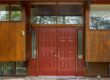 Red double entry doors with glass sidelights on a mid-century style wood exterior home.