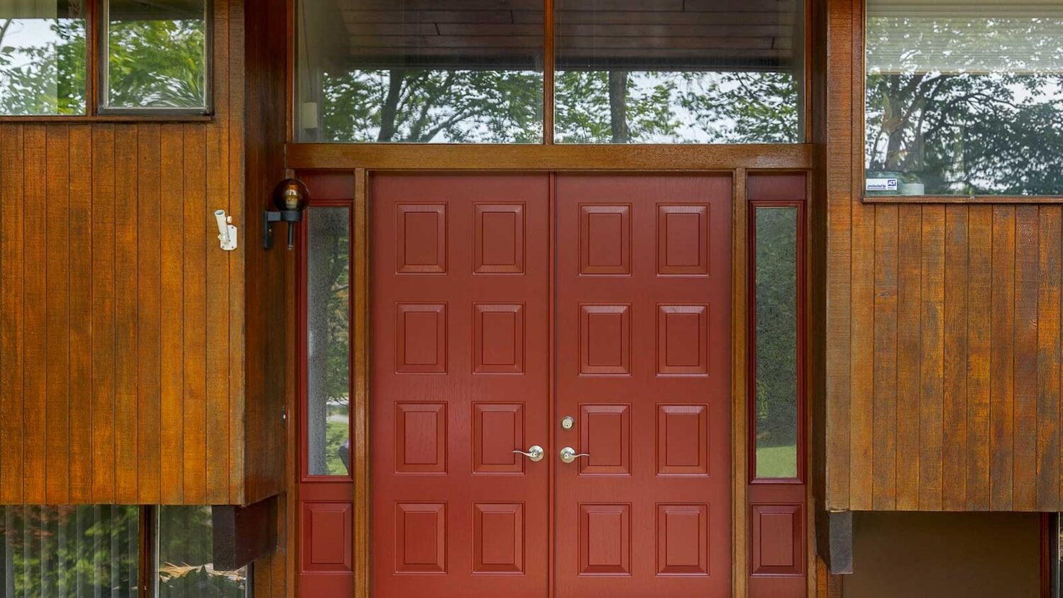 Red double entry doors with glass sidelights on a mid-century style wood exterior home.