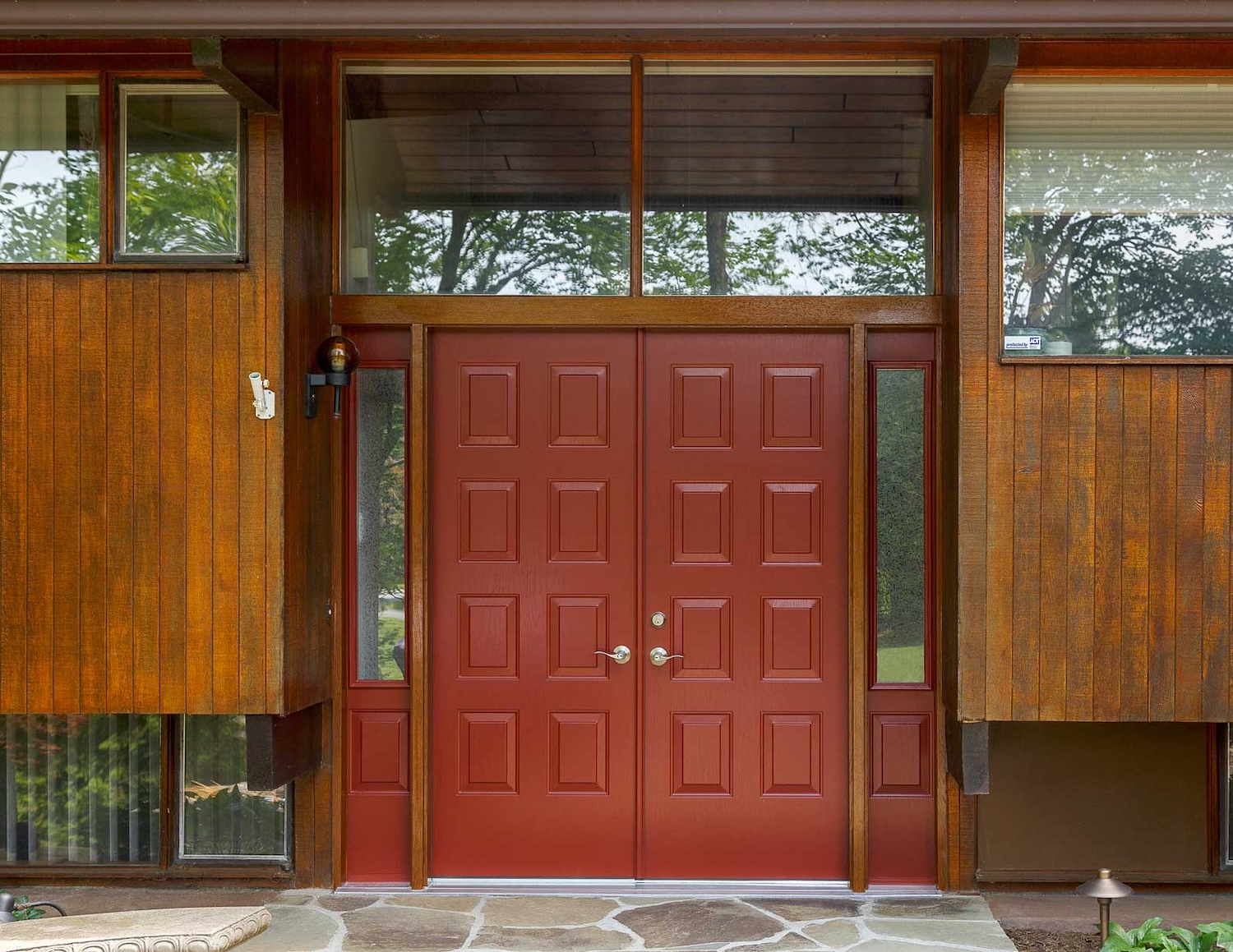 Red double entry doors with glass sidelights on a mid-century style wood exterior home.