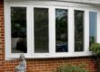 White bow window installed on a red brick home with four large glass panels.