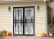 Decorative black wrought iron security doors on a light yellow home with pumpkins outside.