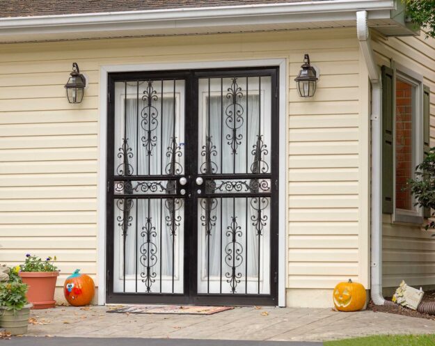 Top Security Doors for Your Patio Protect Your Home With Style and Strength Decorative black wrought iron security doors on a light yellow home with pumpkins outside.